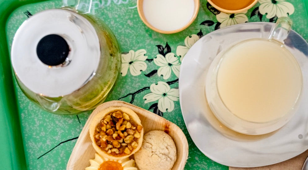 Tea-making setup with teapot, cups, and snacks on a floral tray